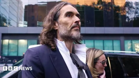 Russell Brand Testifies in High-Stakes Trial as Iran Denies Kuwait Plot; Toman and Gold Edge Higher